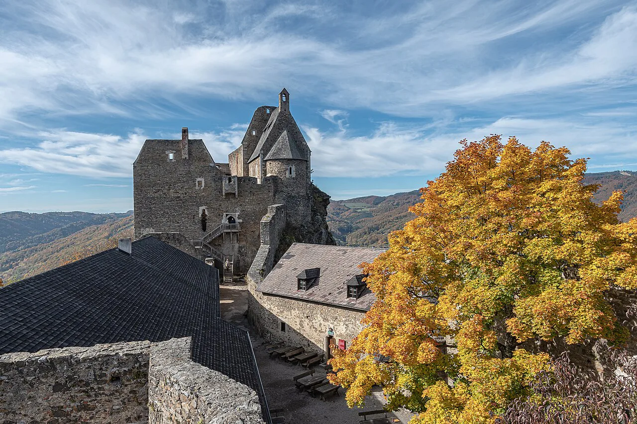 Stone keep and courtyard buildings of Aggstein Castle ruins with autumn trees.