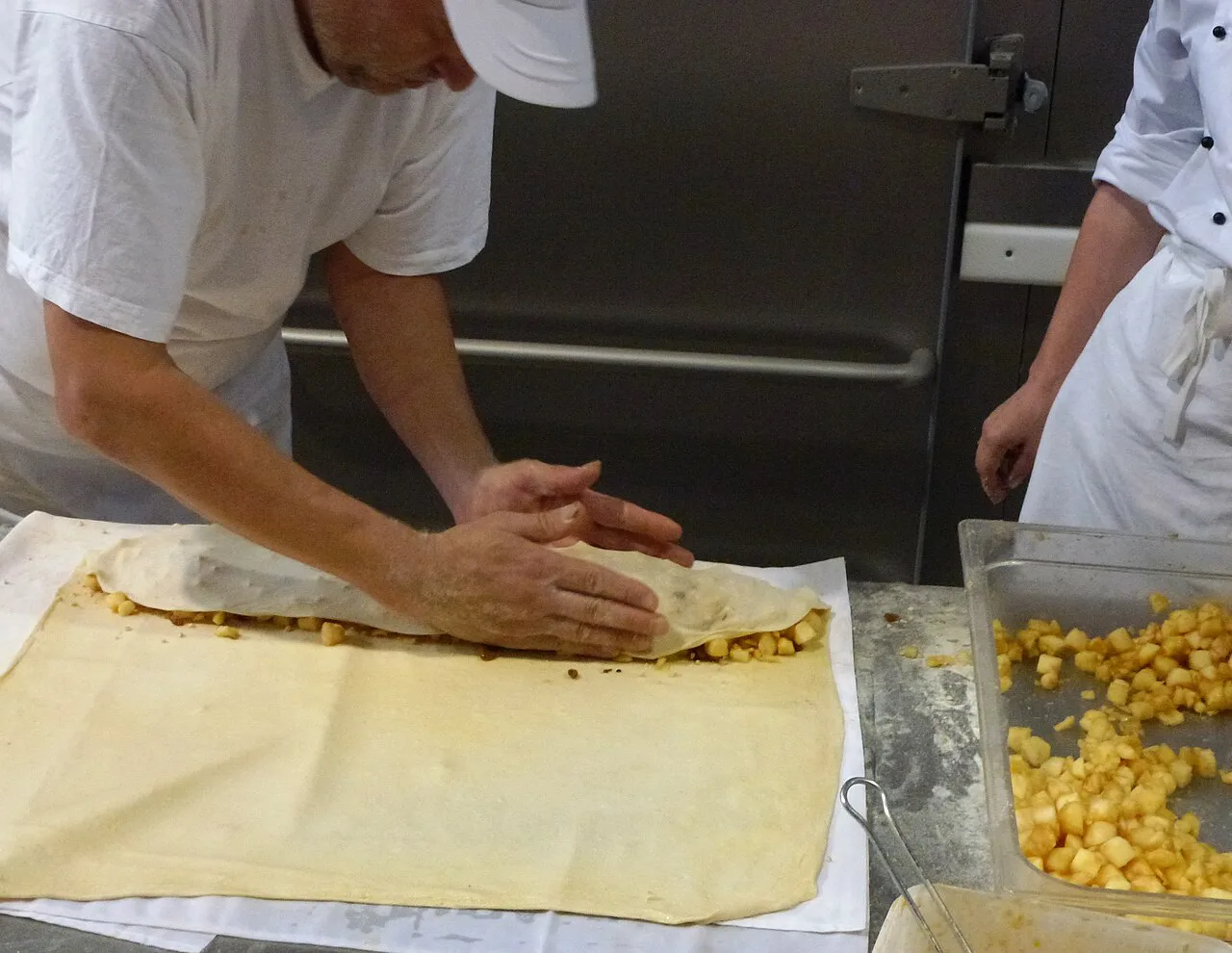 A baker rolling apple strudel dough around its filling in a bakery.