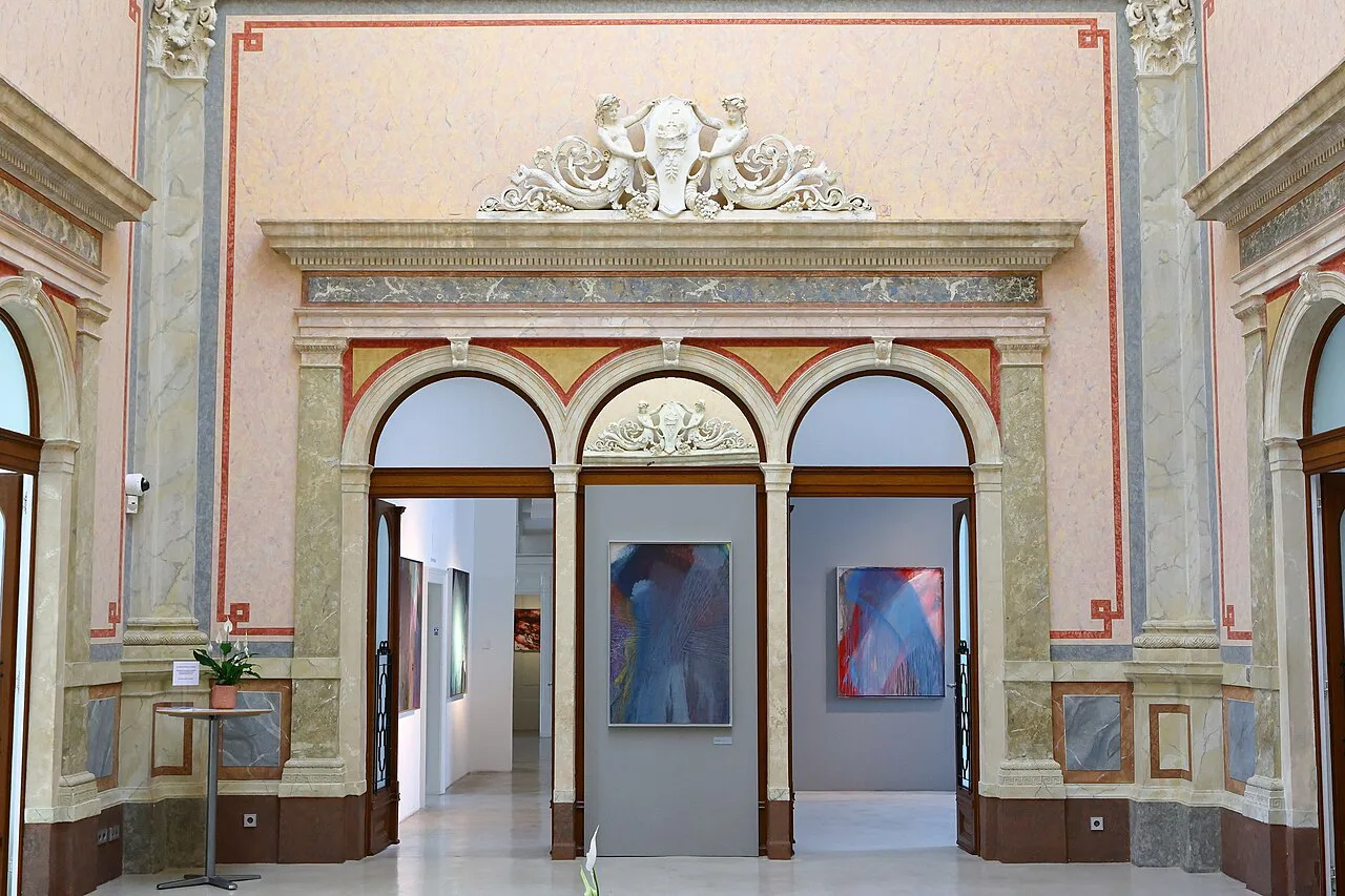 Paintings displayed beneath ornate arches inside the Arnulf Rainer Museum.