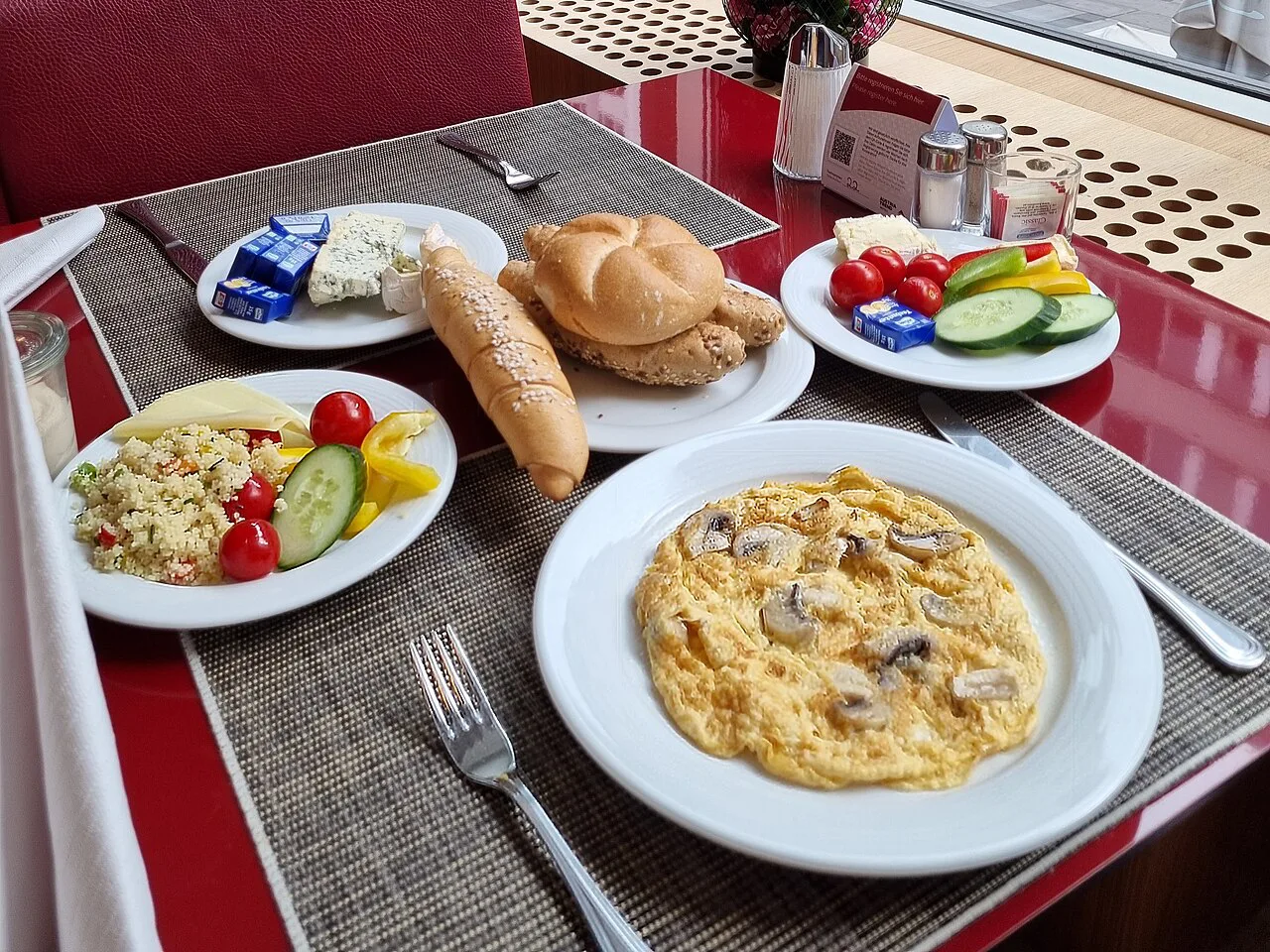 A continental breakfast with rolls, scrambled eggs, cheese and fresh vegetables.