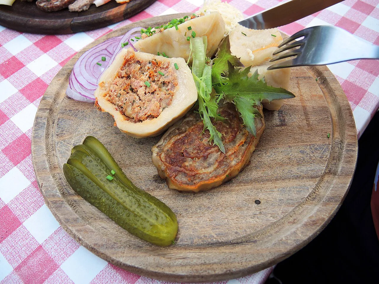 A Heuriger plate of sliced meat-filled dumpling, meat roll, onion and pickled gherkin in Austria.