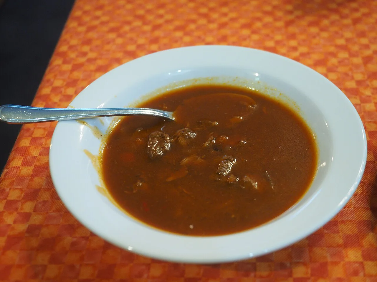 A bowl of goulash in a rich paprika-red sauce.