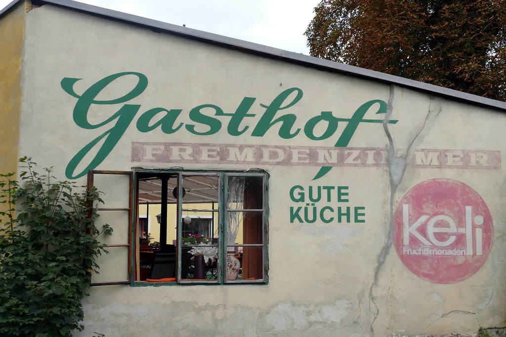 A painted Gasthof sign advertising good cooking on a building in Linz.