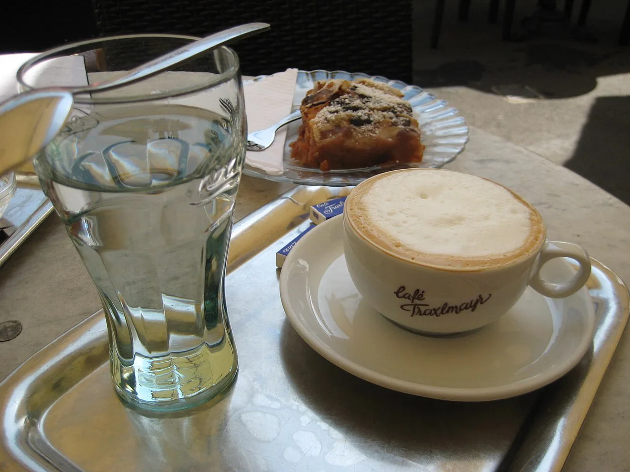 A coffee, glass of water and pastry on the terrace of Café Traxlmayr in Linz.