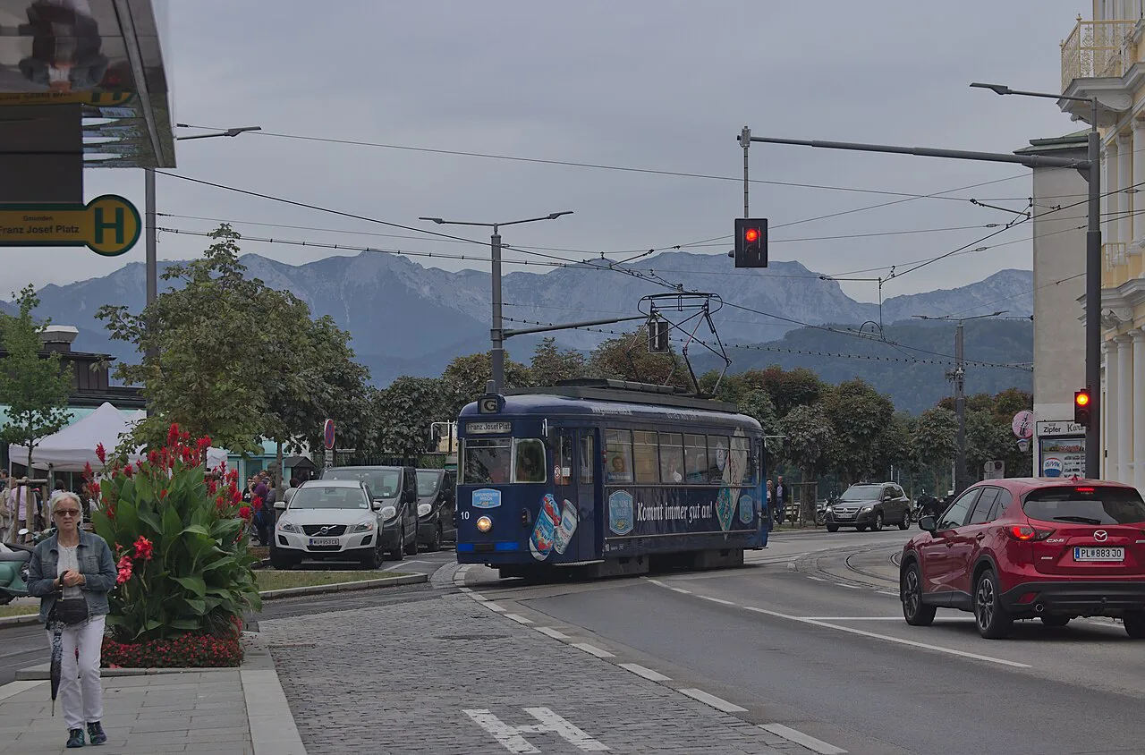 A tram on Gmunden's Esplanade at Franz-Josef-Platz, with mountains beyond.