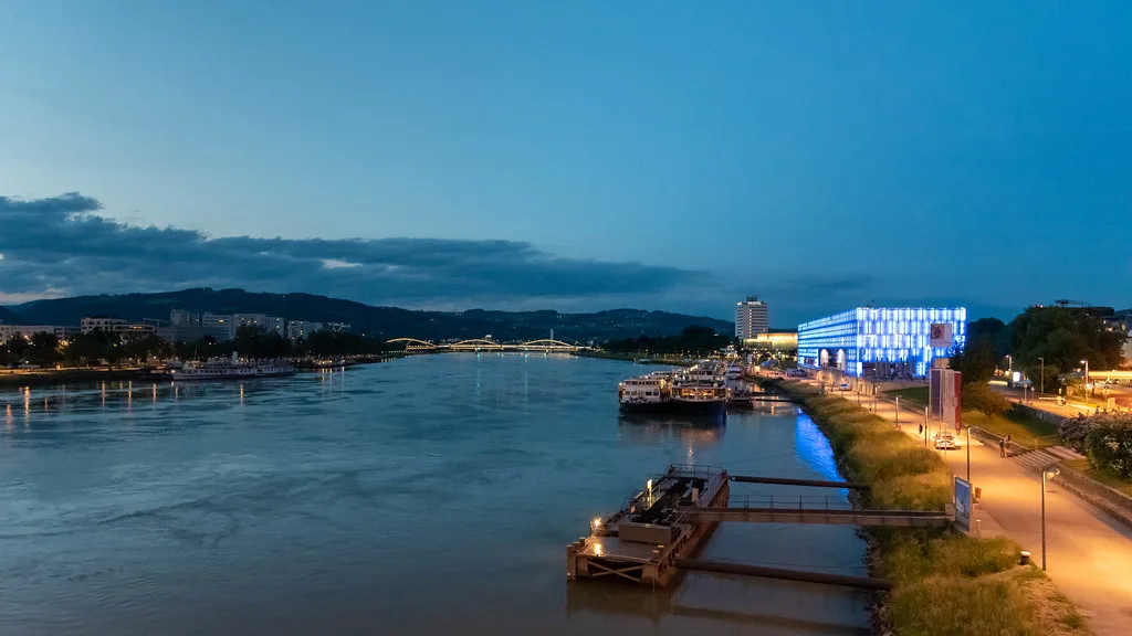 The Danube at dusk in Linz, with the Lentos Art Museum lit blue and river boats moored.