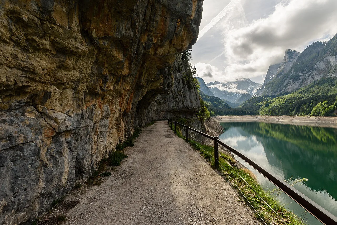 A lakeside path cut beneath a rock overhang at the Vorderer Gosausee.