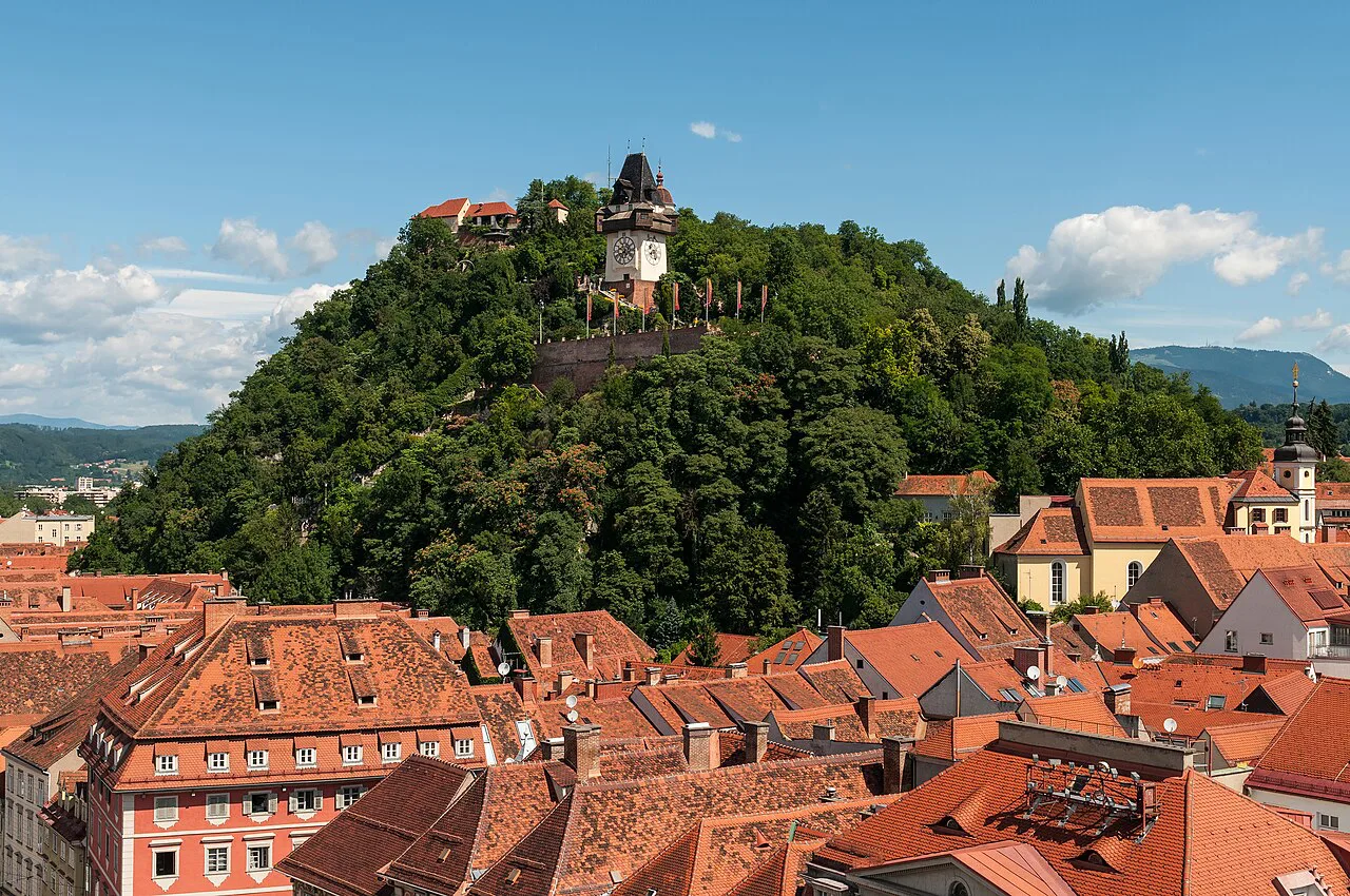 The Schlossberg and its clock tower above Graz's old-town roofs, seen from the town hall spire.