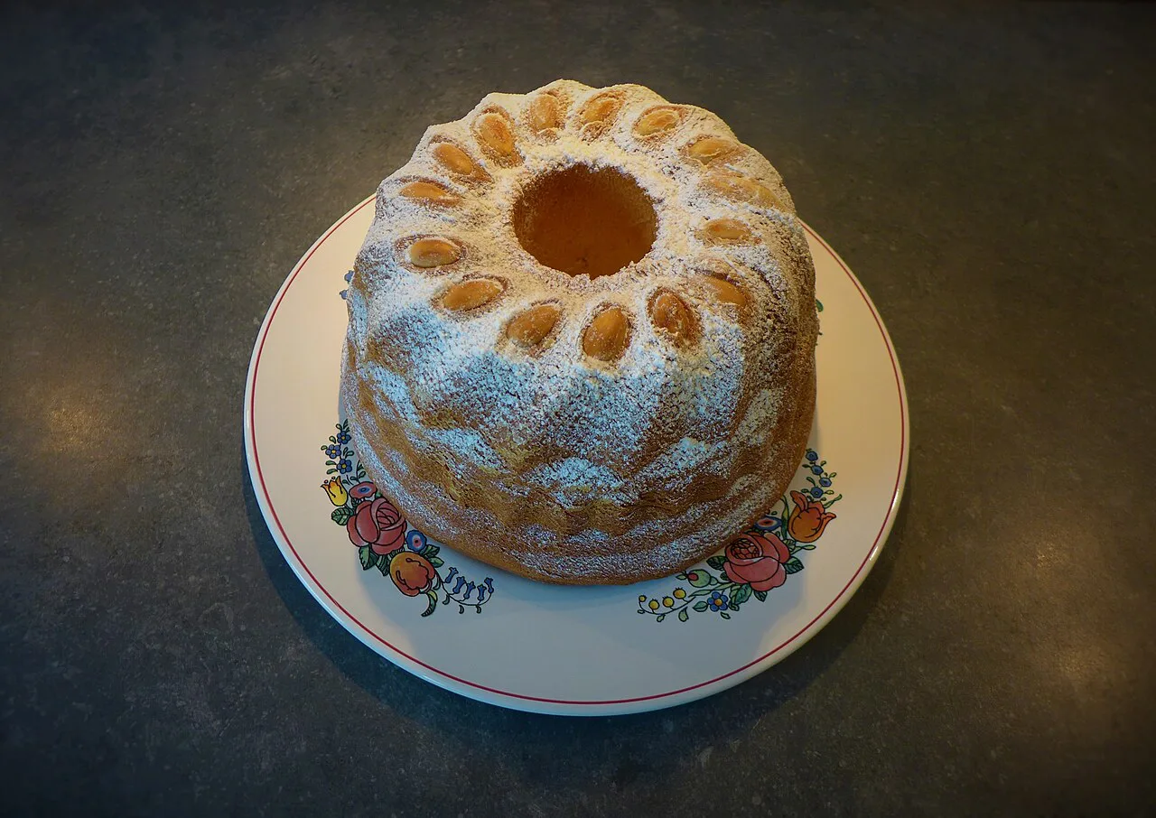 A Gugelhupf topped with almonds and icing sugar on a decorated plate.