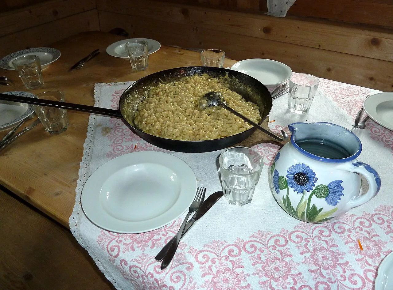 Pinzgauer Kasnocken in a large iron pan on a table set for sharing.