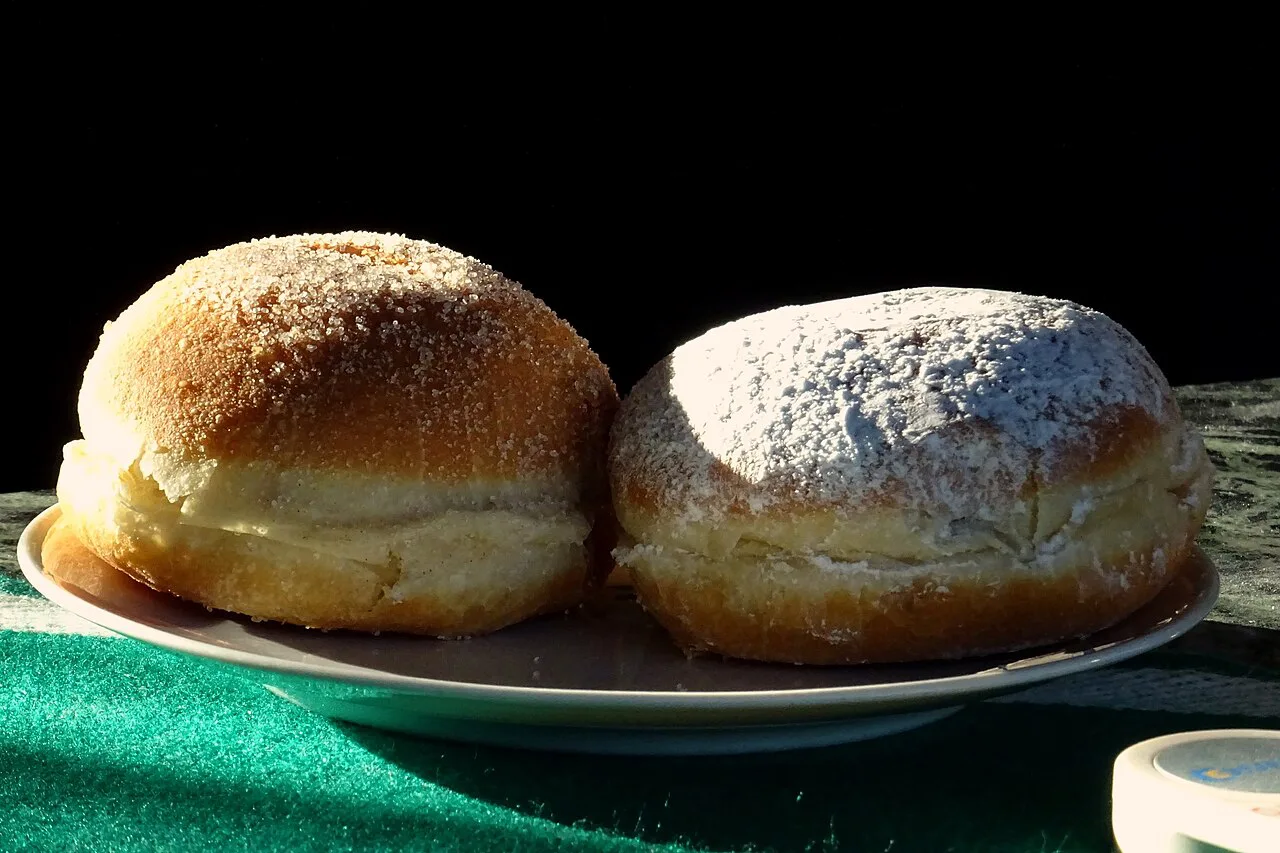Two sugar-dusted Krapfen doughnuts on a plate.
