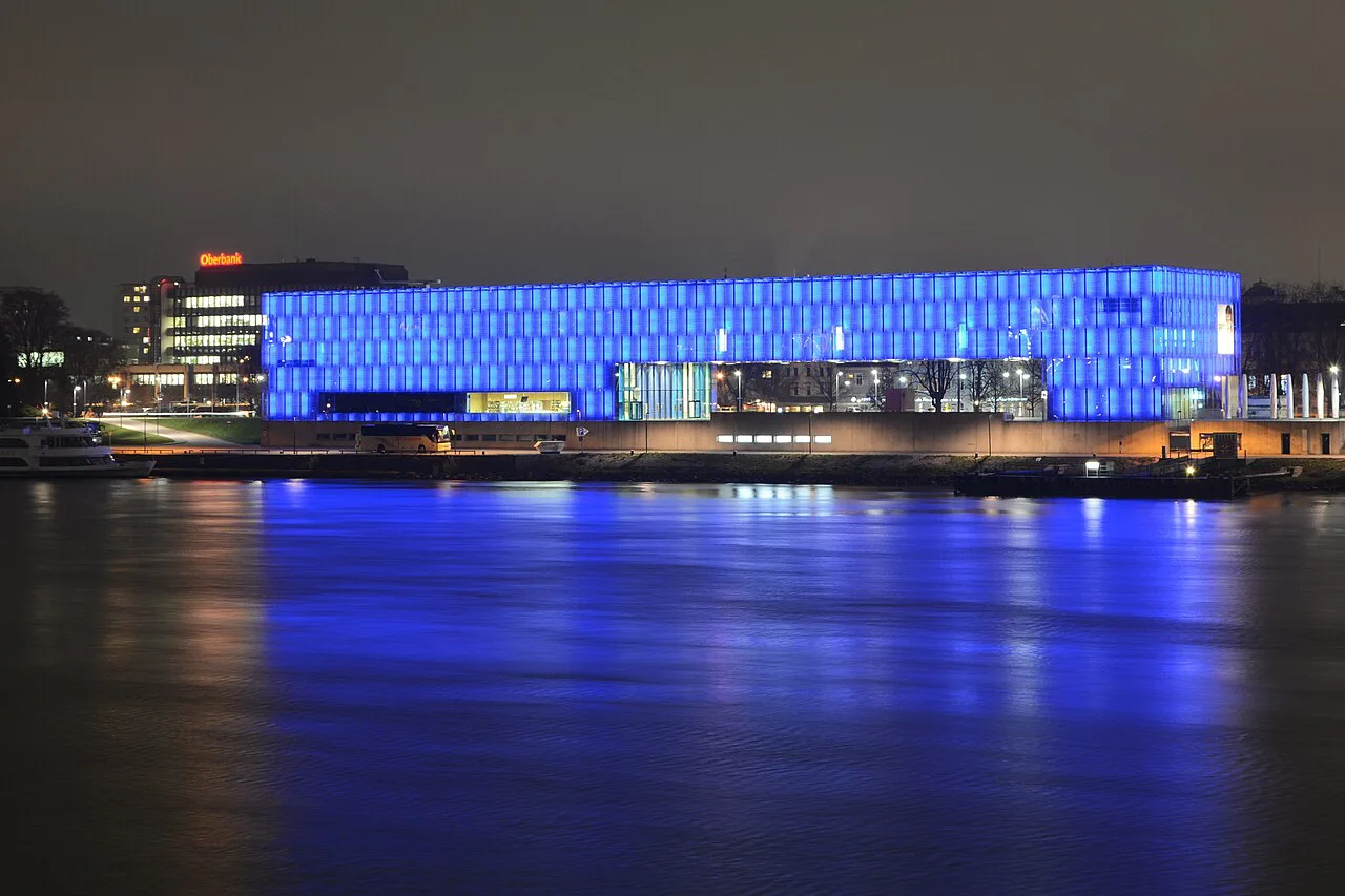 The Lentos Art Museum glowing blue at night beside the Danube in Linz.