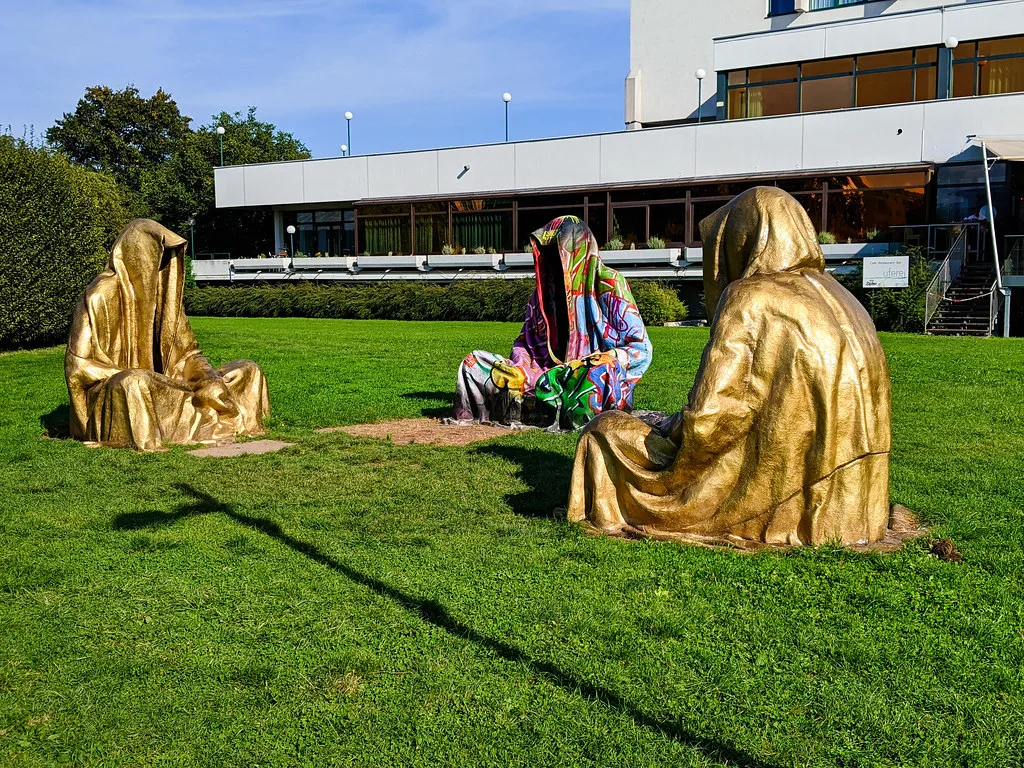Golden hooded sculptures on a lawn beside the Danube in Linz.
