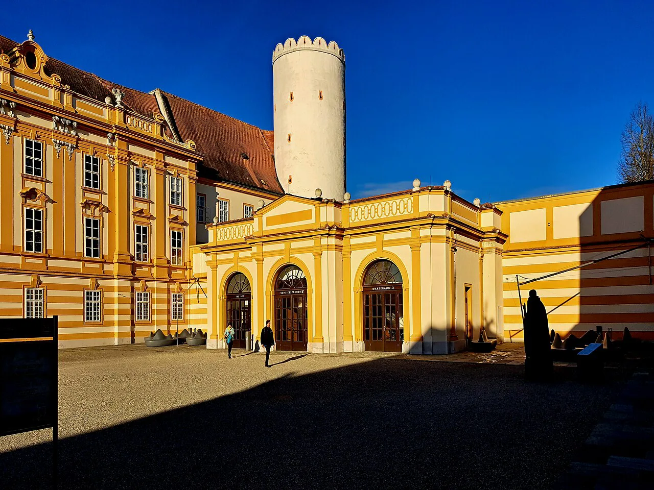 Arcaded gateway and white tower in a courtyard of Melk Abbey.