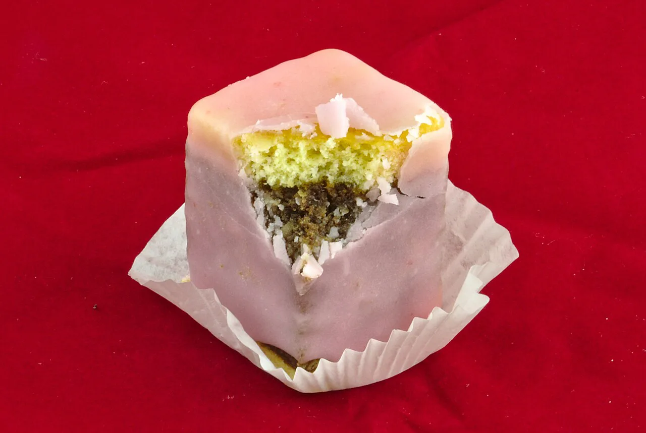 A bitten Punschkrapfen from Ritz in a paper case, showing its layered filling.