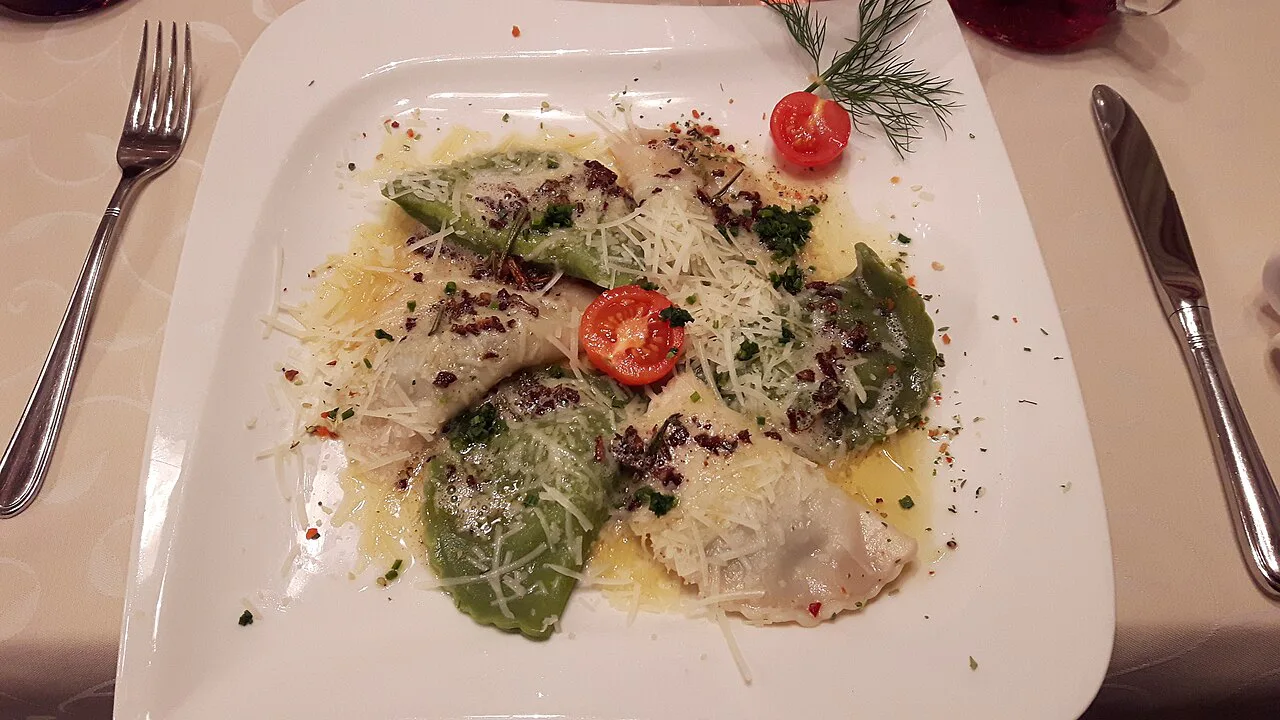 A plate of white and green Schlutzkrapfen with a tomato garnish.