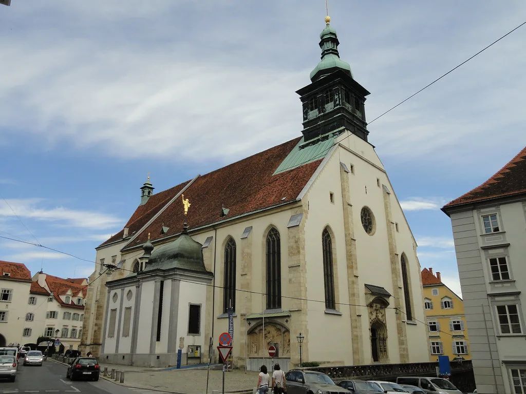 The white facade and green-domed tower of Graz Cathedral in the old town.