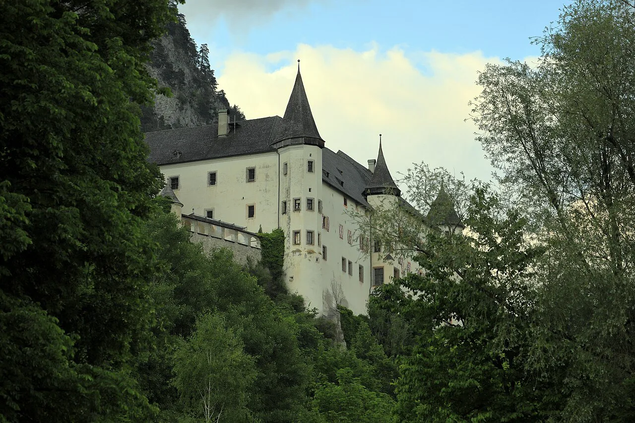 Schloss Tratzberg seen from the road below, framed by trees and cliffs.