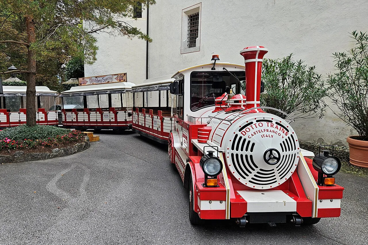 The Schloss Tratzberg road train, a red-and-white Dotto tourist train, parked beside a white-walled building.