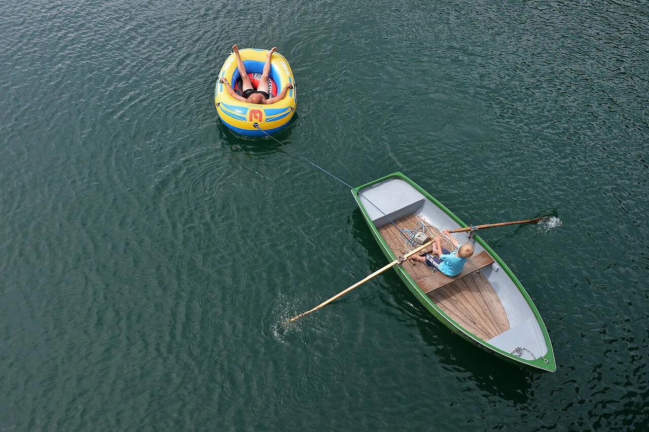 A rowing boat towing an inflatable across the clear water of the Weissensee at Techendorf.