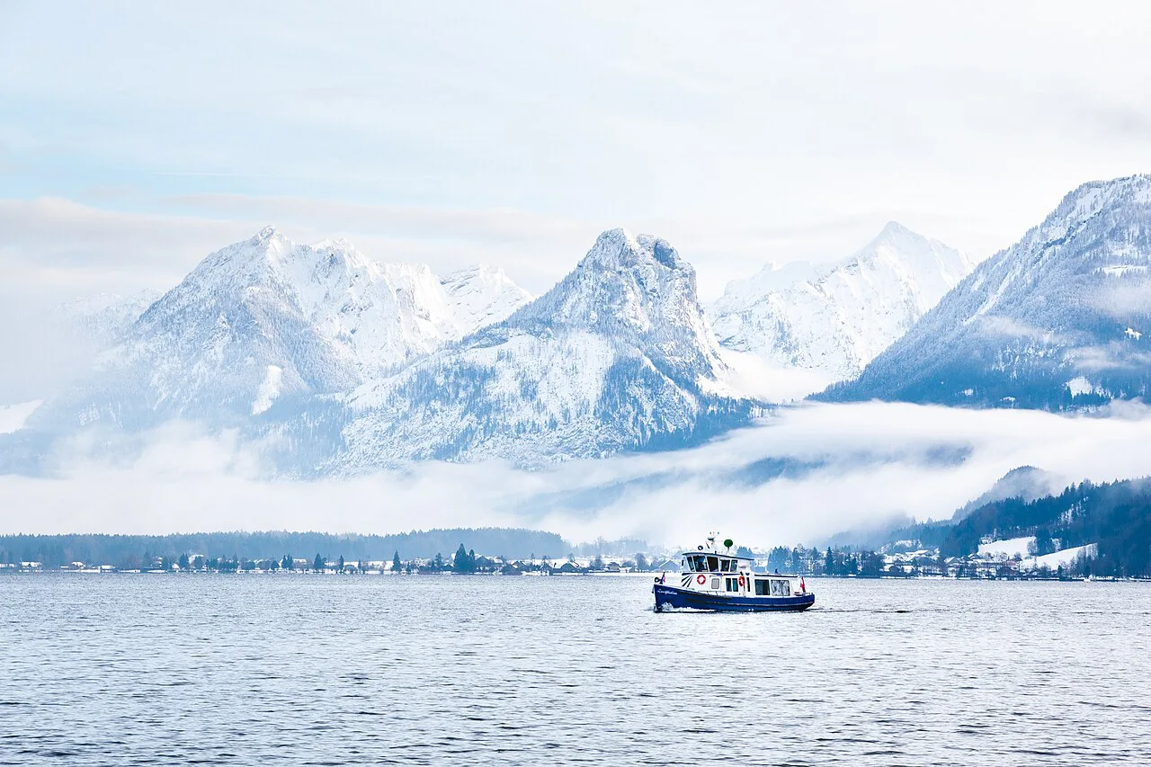 A boat on the Wolfgangsee below snow-covered mountains.